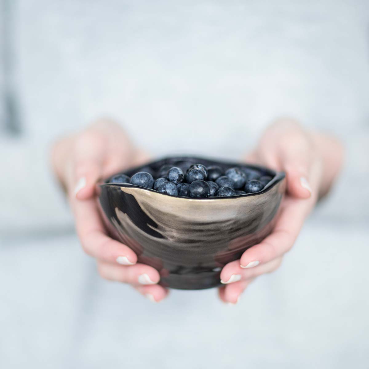 reese - annavasily handmade small blue bowl with gold highlights and blueberries offered by a woman.