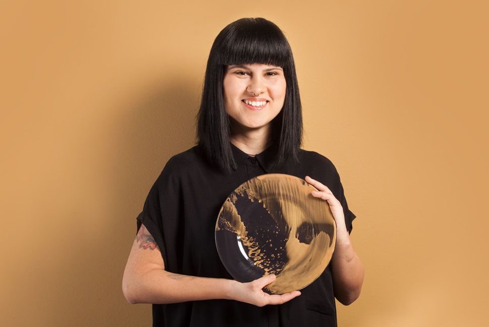 Girl dressed in black with black hair and bangs holding a designer dinner plate Vossi by AnnaVasily with a yellow background.