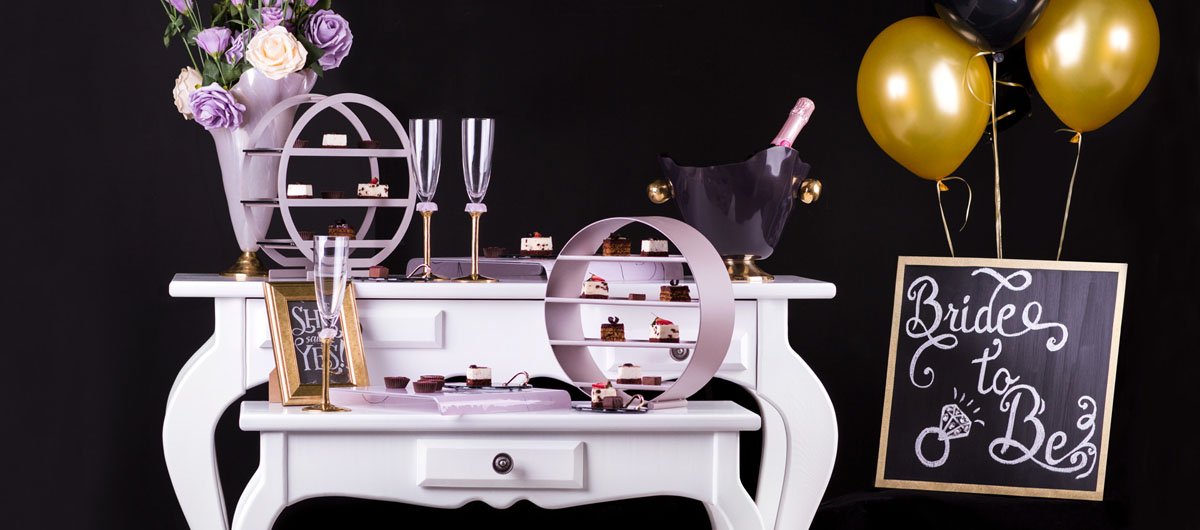 Unique partyware for a Bachelorette party with round high tea stands, champagne glasses and a champagane bucket on a white table with a black background.