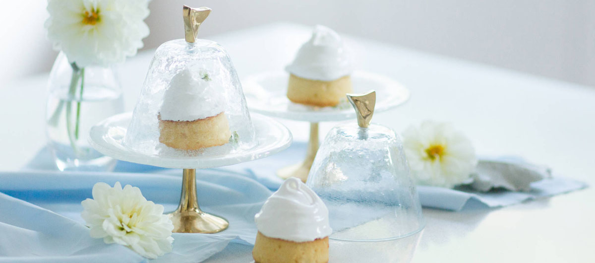 Cute Small White Glass Cake Holder With a Glass Cover Lid and a Bronze Pedestal by AnnaVasily With Other Cake Stands With Petit Fours on a Blue Tablecloth.