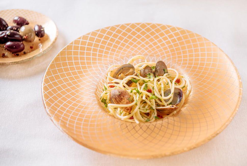 Gold wide-rimmed pasta bowl with pasta and a matching side plate wih olives.