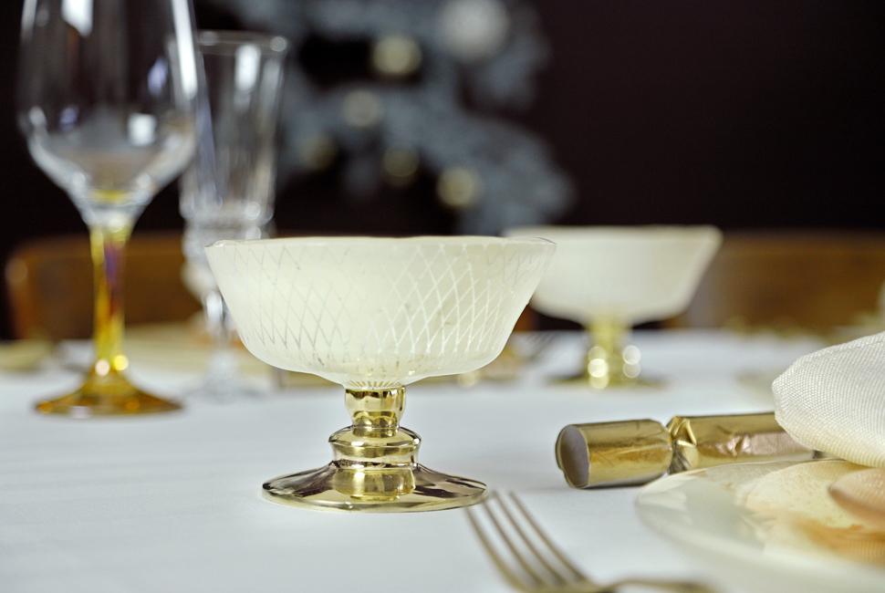 Beige trifle bowl Mardi with a bronze pedestal on a table with a coral dinner set and gold accents.