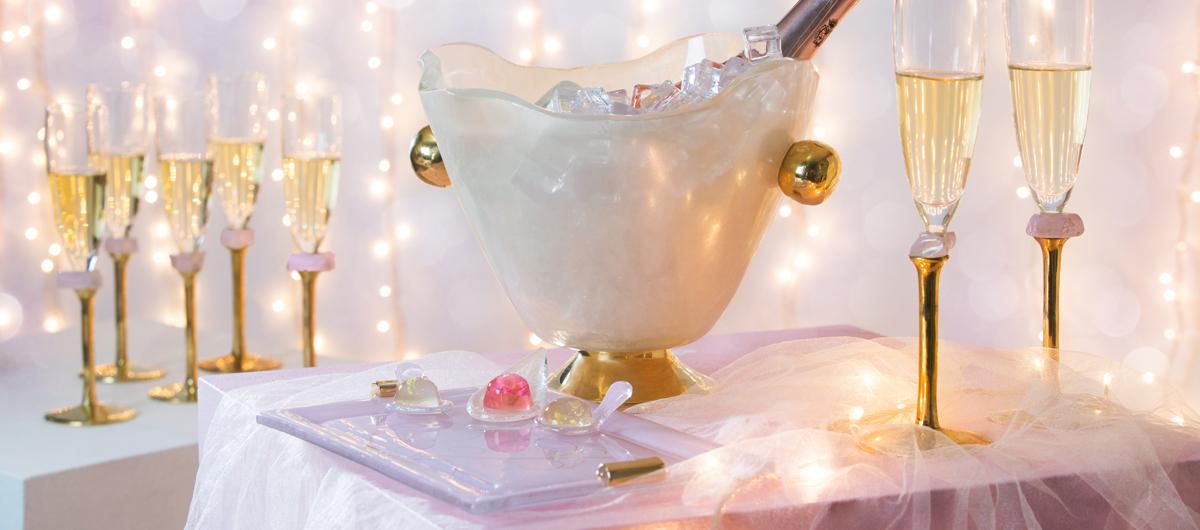 Pink New Year's Party Table Setting with gold champagne glasses, an elegant ice bucket with champagne and a charger plate with canape spoons with jello shots.