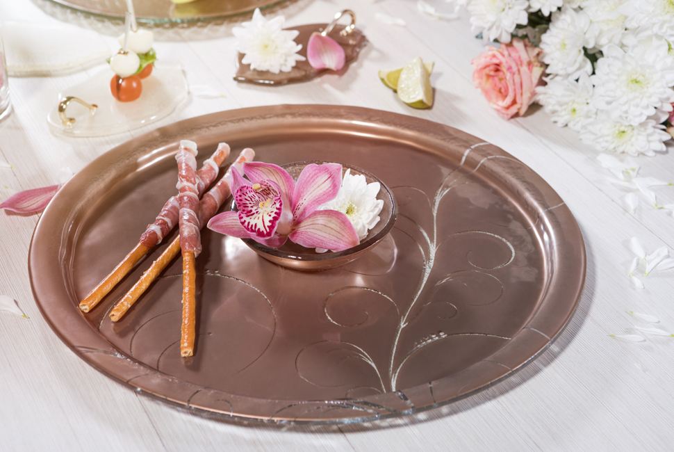 Metallic brown glass serving platter with a dipping bowl with breadsticks wrapped in bacon on a white tablecloth.