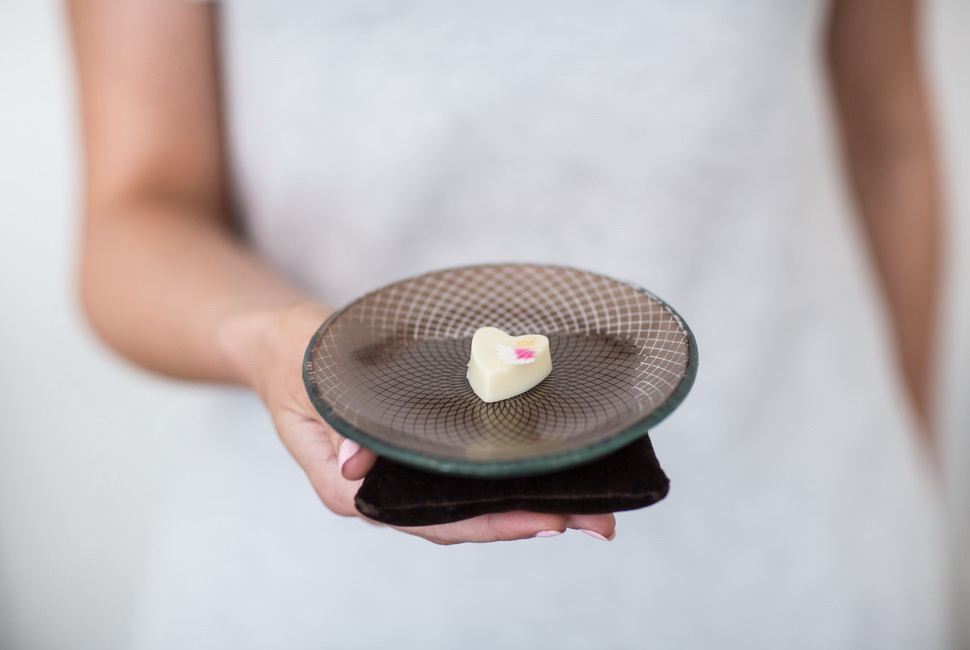 Woman's hands holding 1 of AnnaVasily's brown cake plates on a pillow with small heartshaped dessert on it