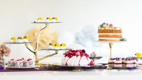 Designer glass cake stands, plates and tall pedestal cake stand by Anna Vasily with lamingtons and a Pavlova.