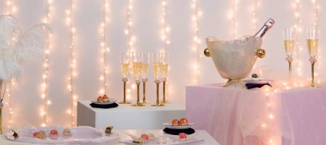 New Year's party table setting with pink new year tableware, champagne glasses and am ice bucket with champagne with a pink background with fairylights.
