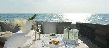A sailboat tablescape with a blue dinner set, a beige blue champagne bucket, 2 champagne glasses and a light blue jewelry box.